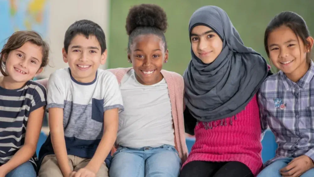 Five smiling children of diverse backgrounds sit together in a classroom.