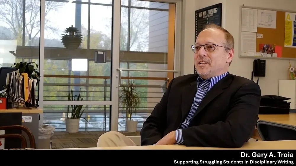 Dr. Gary A. Troia smiles while wearing glasses and a suit jacket in an office setting.
