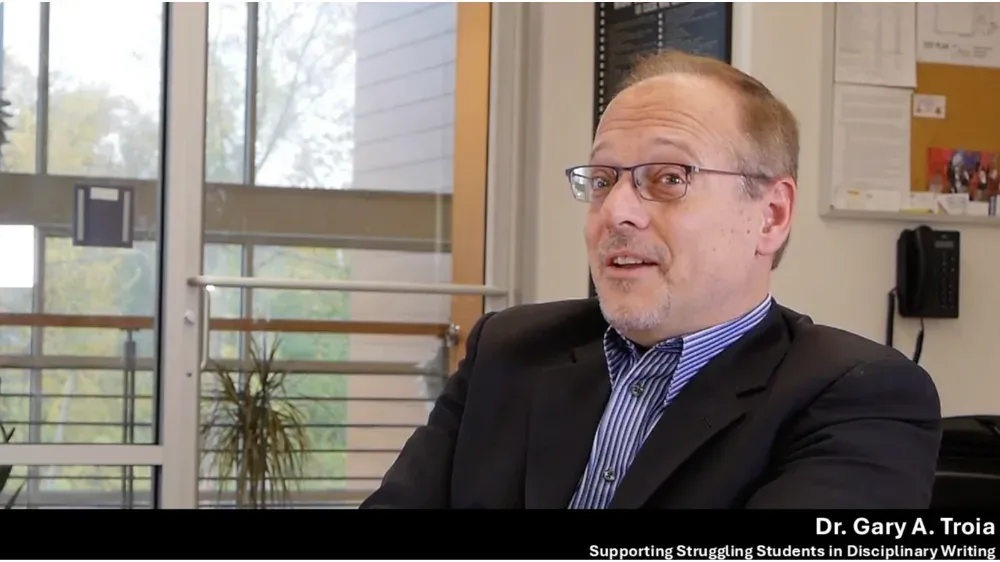 Dr. Gary A. Troia, wearing glasses and a suit, speaks during a discussion.