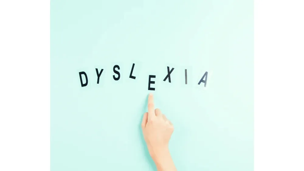 The word DYSLEXIA spelled out in block letters against a light blue background, with a finger pointing to the letter E.